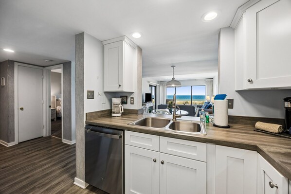 A modern kitchen with a dishwasher, double sink, and a view of the ocean.