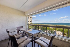 A balcony with a table and chairs, overlooking a beach and ocean.
