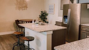 A kitchen with a central island, bar stools, a refrigerator, and pendant lighting.