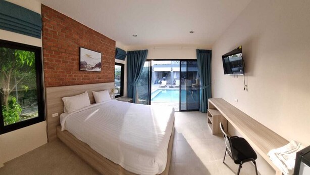 Una habitación de hotel moderna con una cama grande, un escritorio, un televisor y vista a una piscina.