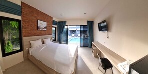 A modern hotel room with a large bed, a desk, a TV, and a view of a swimming pool. - Bests village & villa (Chalong)
