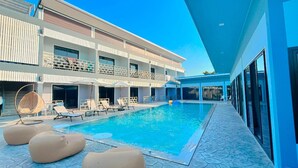 Un hotel moderno con piscina, sillas de descanso y una zona de estar cubierta.