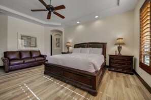 A bedroom with a large bed, a leather sofa, a nightstand, and a ceiling fan.