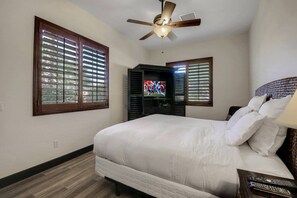 A bedroom with a bed, a ceiling fan, and a television.