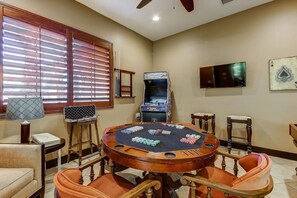 Ein Zimmer mit einem Pokertisch, Stühlen, einem Fernseher und einem Spielautomaten.