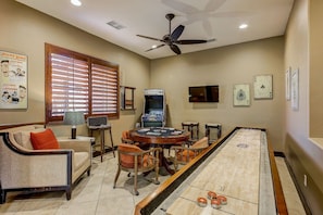 A room with a shuffleboard table, a sofa, a television, and a ceiling fan.