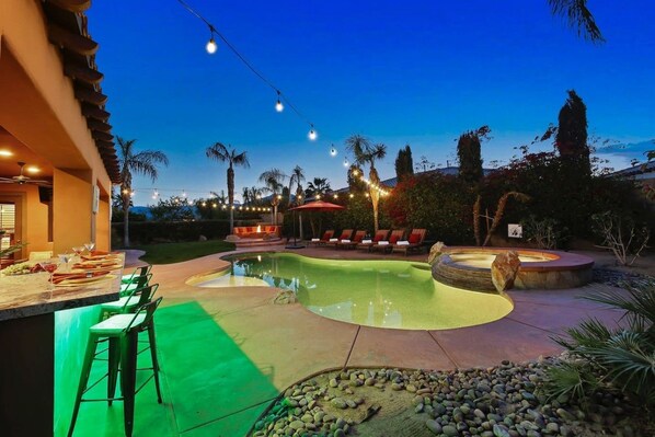A swimming pool with a sunken hot tub, outdoor bar, and lounge chairs.