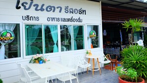 A coffee shop with a sign in a foreign language, outdoor seating with white chairs, and a potted plant. - Yenta Resort (Chumphon)