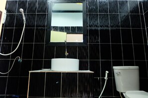 A bathroom with a black tiled wall, a white sink, a mirror, and a toilet. - Yenta Resort (Chumphon)