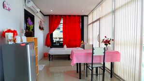 A compact hotel room with a bed, a dining table with a checkered tablecloth, a refrigerator, and a window with vertical blinds. - Yenta Resort (Chumphon)