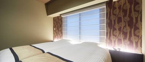 A hotel room with a large bed, a window with blinds, and patterned curtains.