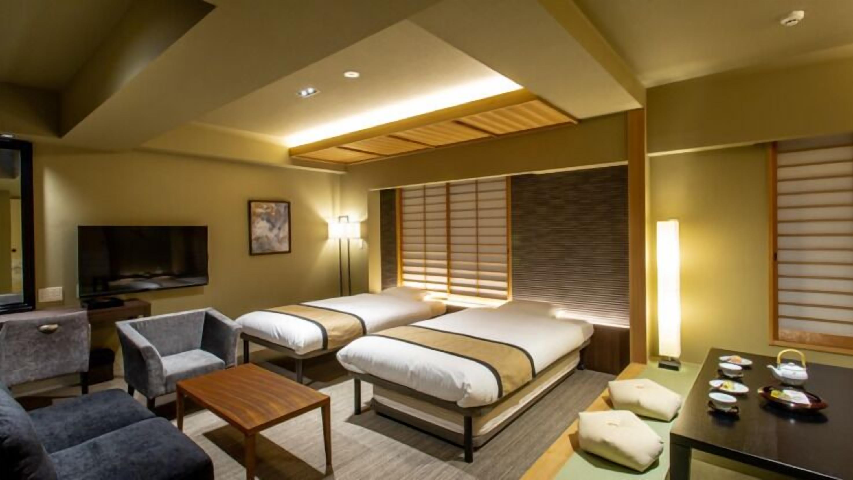 Une chambre d’hôtel avec deux lits, une télévision, un canapé, une table et une fenêtre avec des stores.