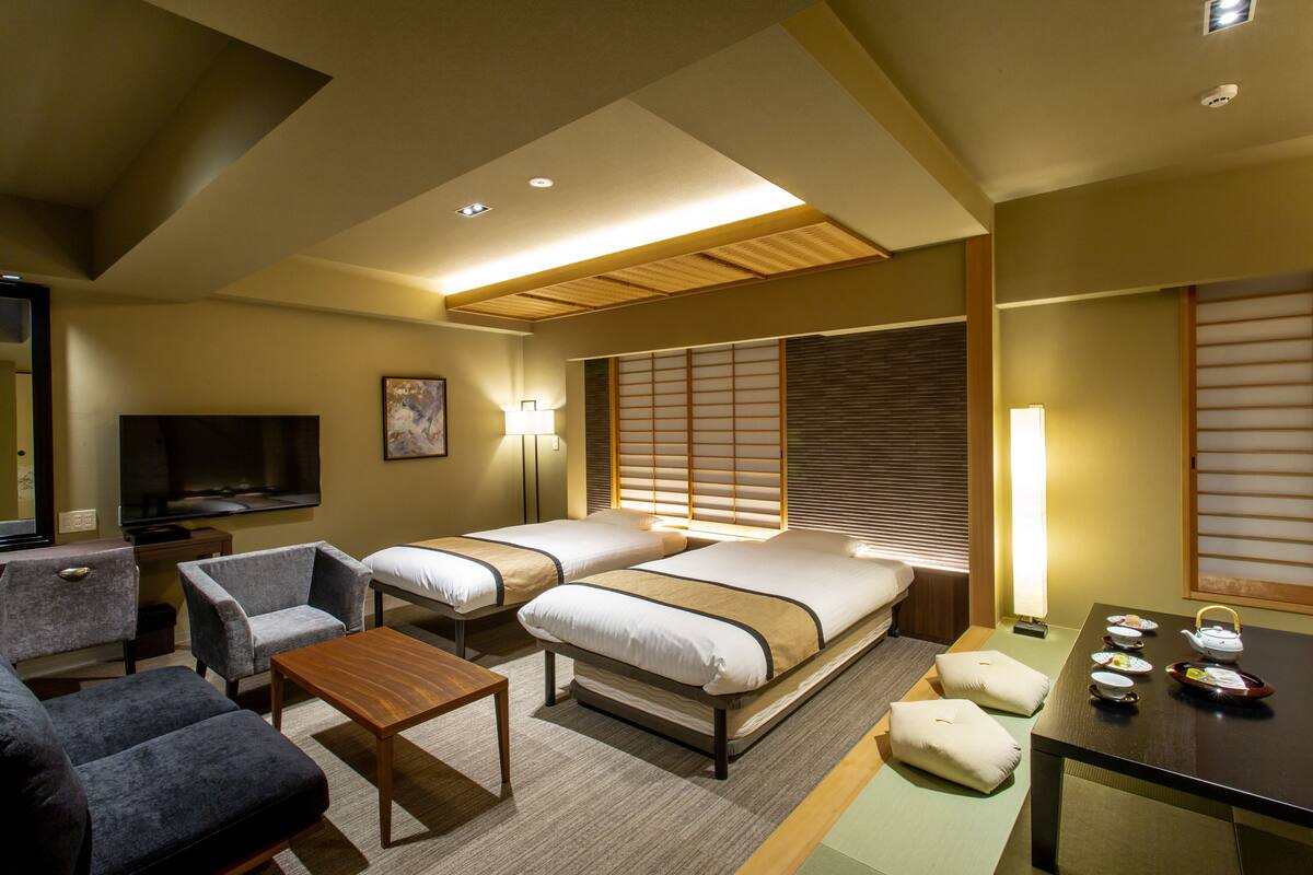 A hotel room with two beds, a TV, a sofa, and a table with tea set.