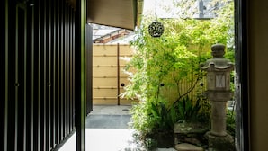Ein traditioneller japanischer Garten mit Bambuszaun, Steinlaterne und Blick auf ein hölzernes Gebäude im Hintergrund.