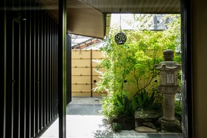 A traditional Japanese garden with a bamboo fence, a stone lantern, and a view of a wooden building in the background.