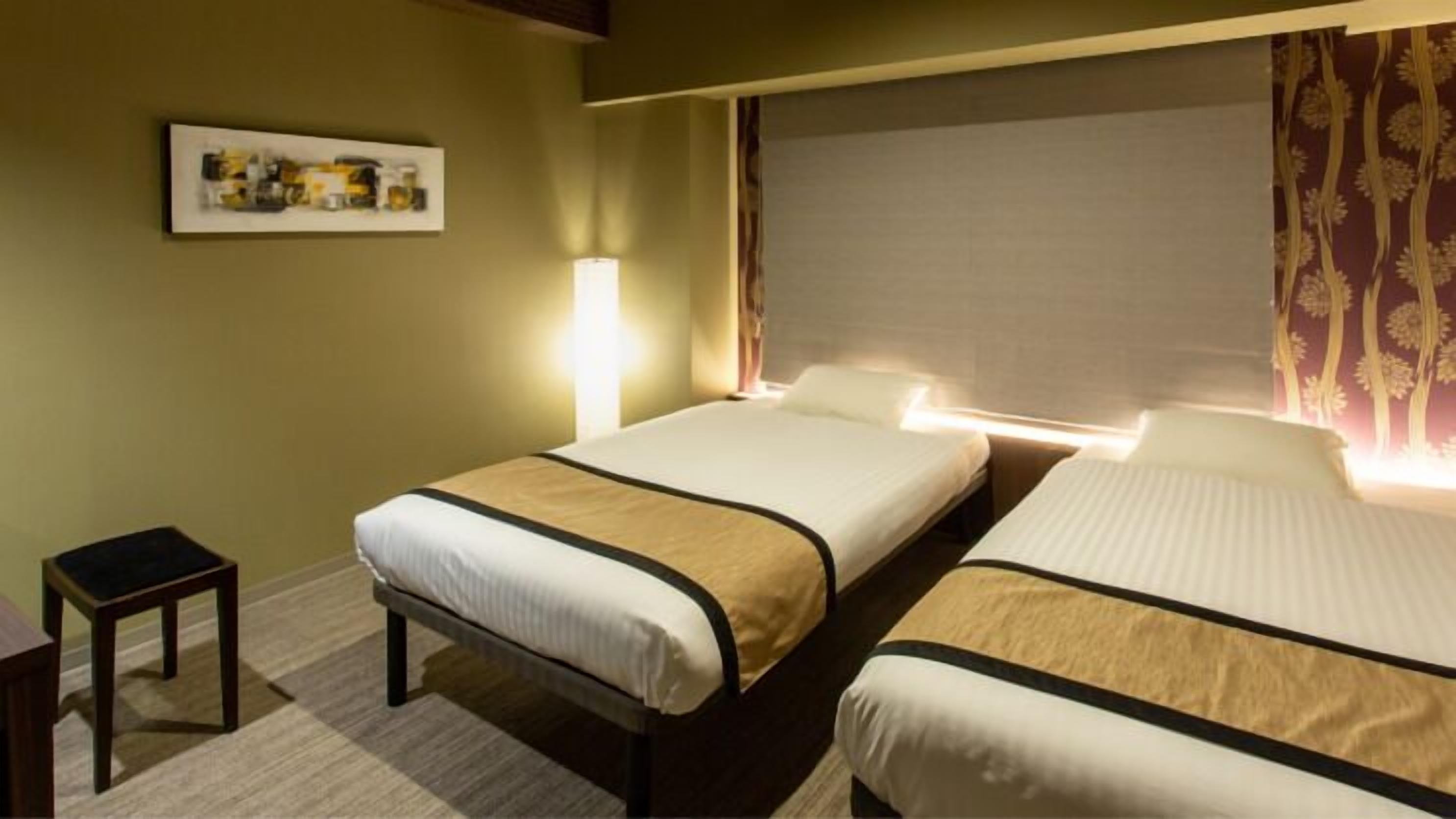 Une chambre d’hôtel avec deux lits, une petite table, une lampe et un tableau encadré au mur.