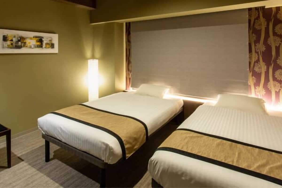 A hotel room with two beds, a small table, a lamp, and a framed picture on the wall.