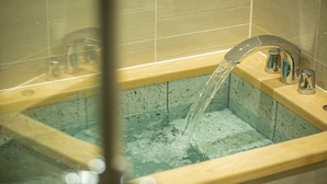 Eine Badewanne mit fließendem Wasser, eine Glastür und ein hölzernes Ablagebrett.