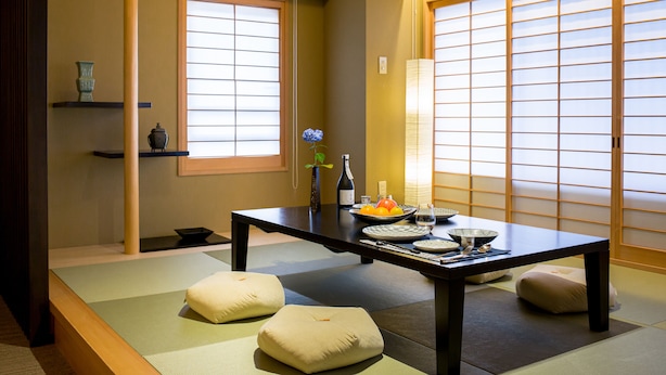 Ein traditioneller japanischer Raum mit Tatami-Boden, niedrigem Tisch, Kissen und Schiebetüren.