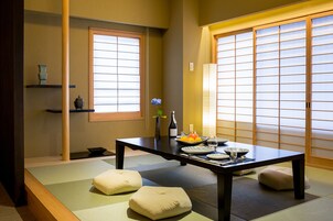 A traditional Japanese room with tatami flooring, a low table, cushions, and sliding doors.