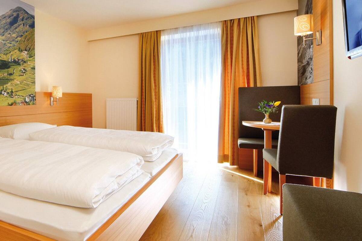 Quarto de hotel com uma cama grande, uma escrivaninha com cadeira, uma televisão e um quadro de uma paisagem na parede.