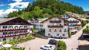 Un village alpin traditionnel, avec des bâtiments à plusieurs étages, des balcons ornés de jardinières et une vue dégagée sur les collines environnantes.