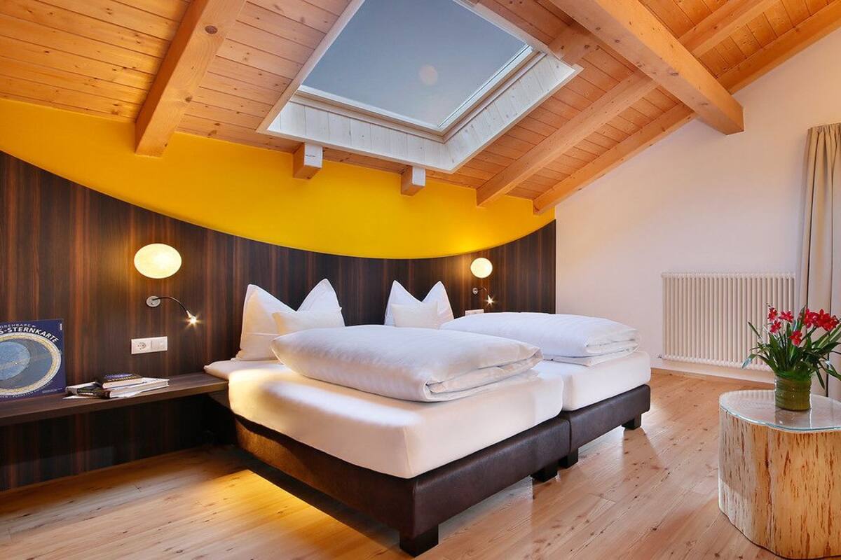 Quarto com cama, sofá, mesa redonda pequena e claraboia.