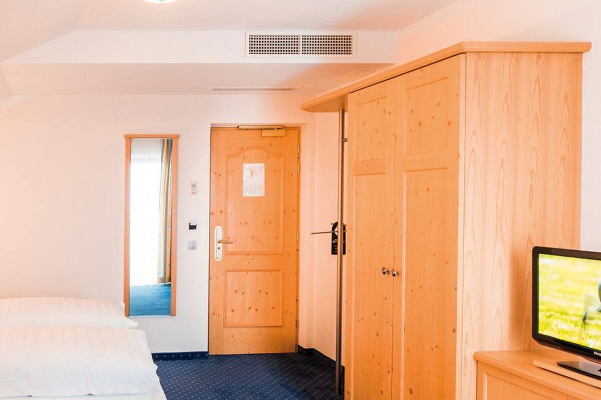 Quarto de hotel com uma cama, televisão e guarda-roupa de madeira.