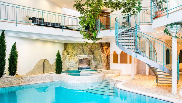Une piscine intérieure dotée d’une cascade centrale, d’un escalier en colimaçon et d’un mur en pierre servant de décor.