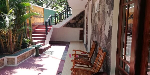 Una escalera que conduce a un segundo piso, sillas de madera afuera y un muro de piedra.