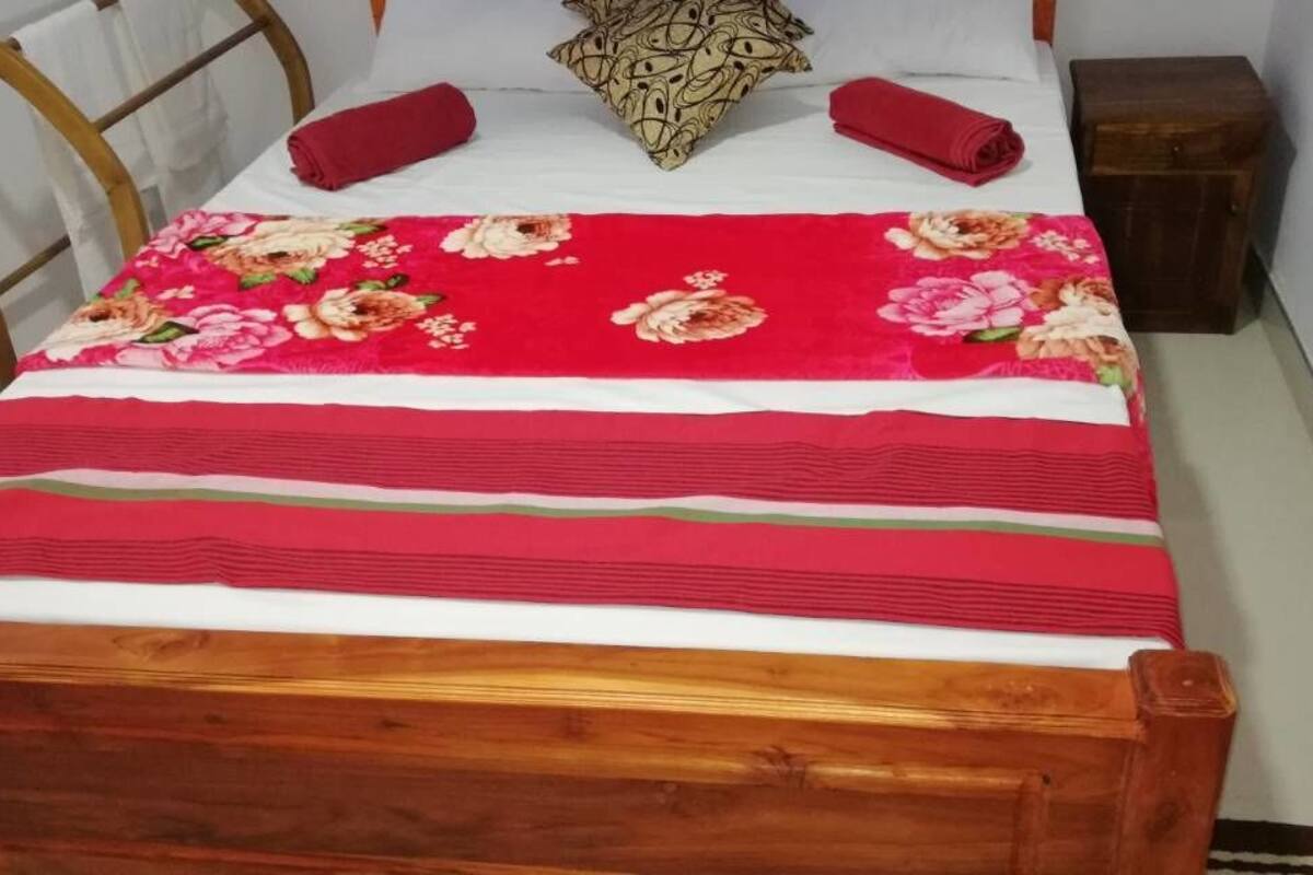Ein Bett mit blumigem Überwurf, zwei Kissen und einem Holz-Kopfteil.