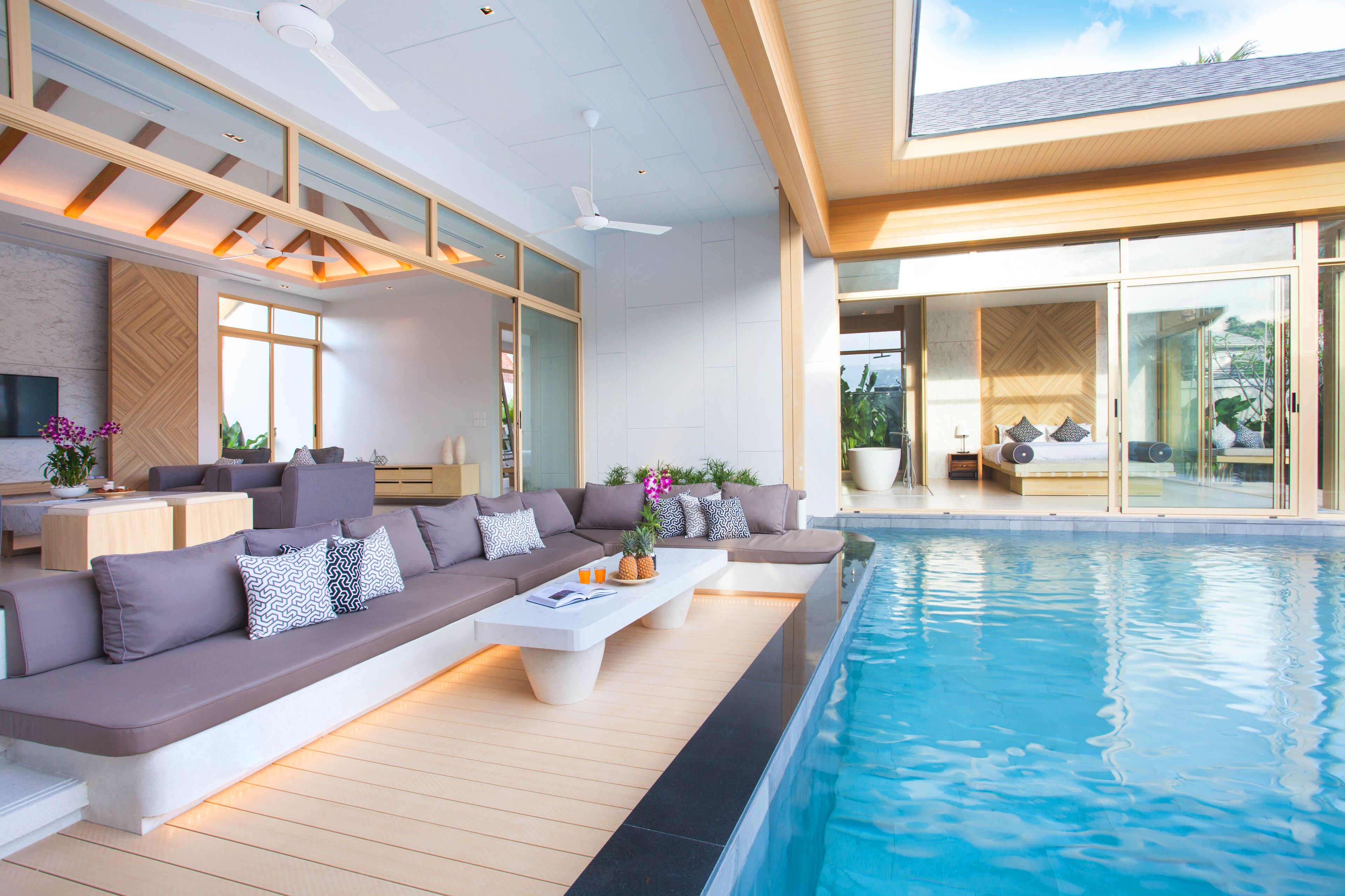A modern indoor pool area with a long, low seating area and a glass-enclosed room in the background.