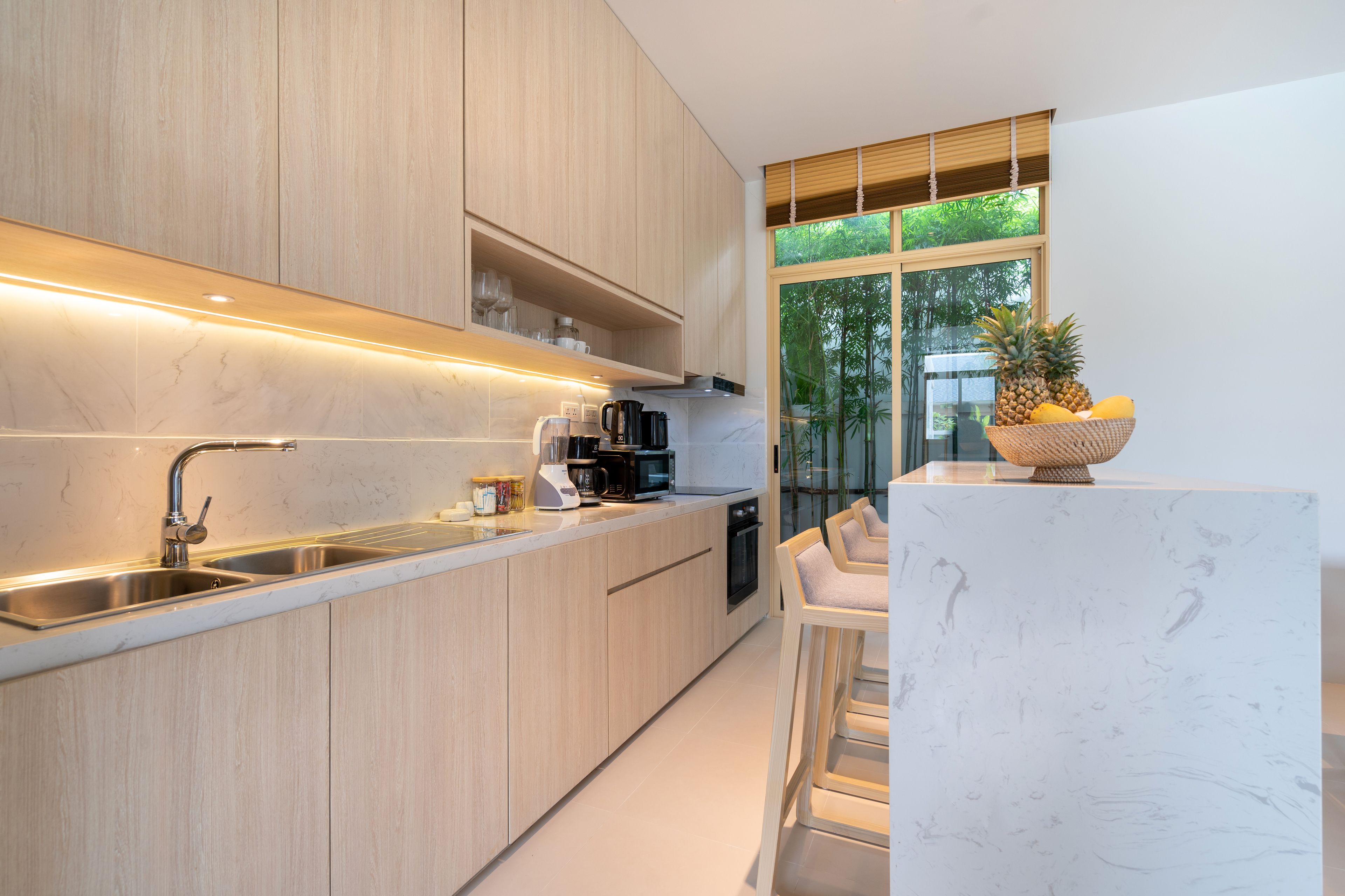 A modern kitchen with wooden cabinets, stainless steel appliances, and a large window with a view of greenery.