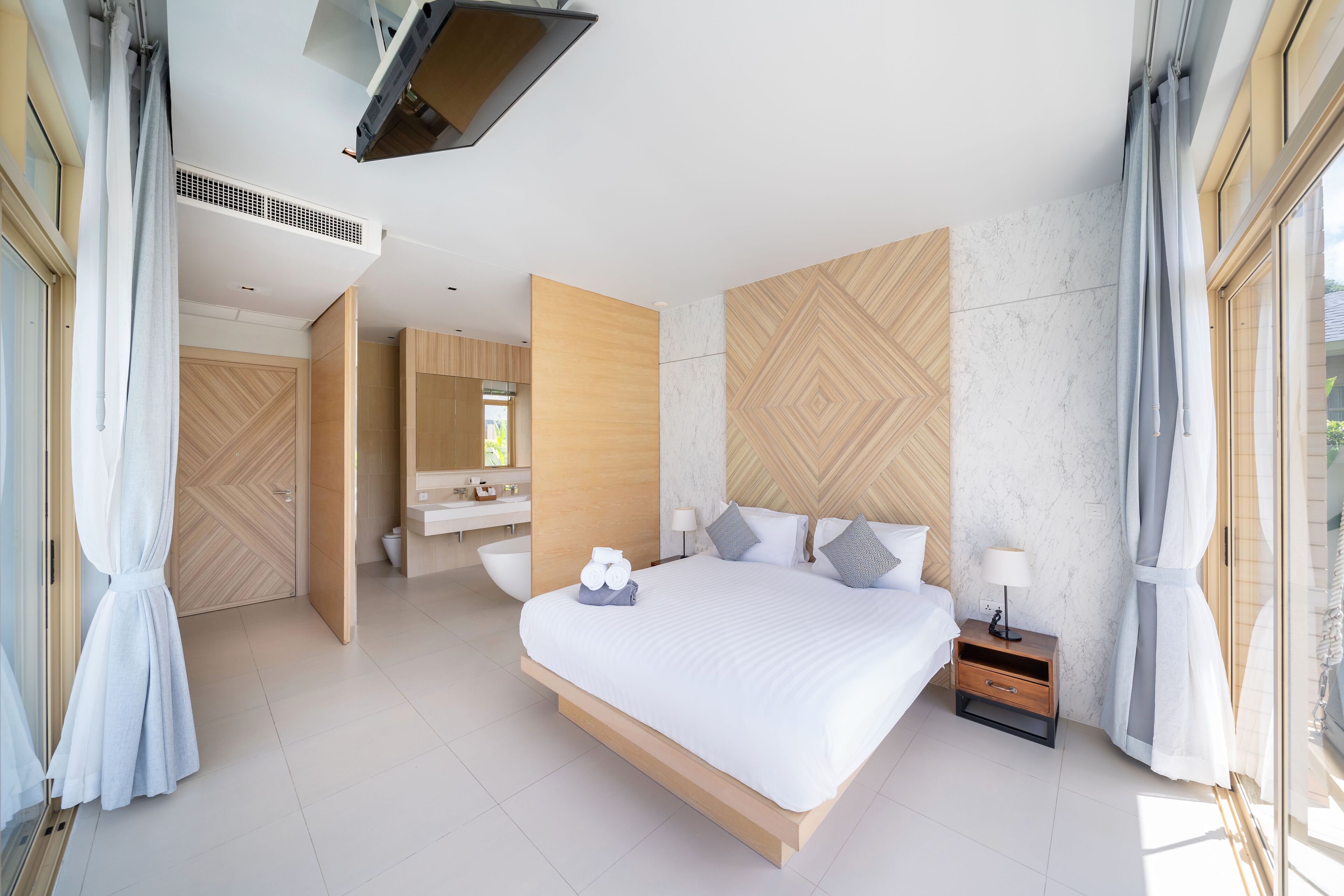 A modern bedroom with a large bed, a nightstand, and a bathroom visible through an open door.