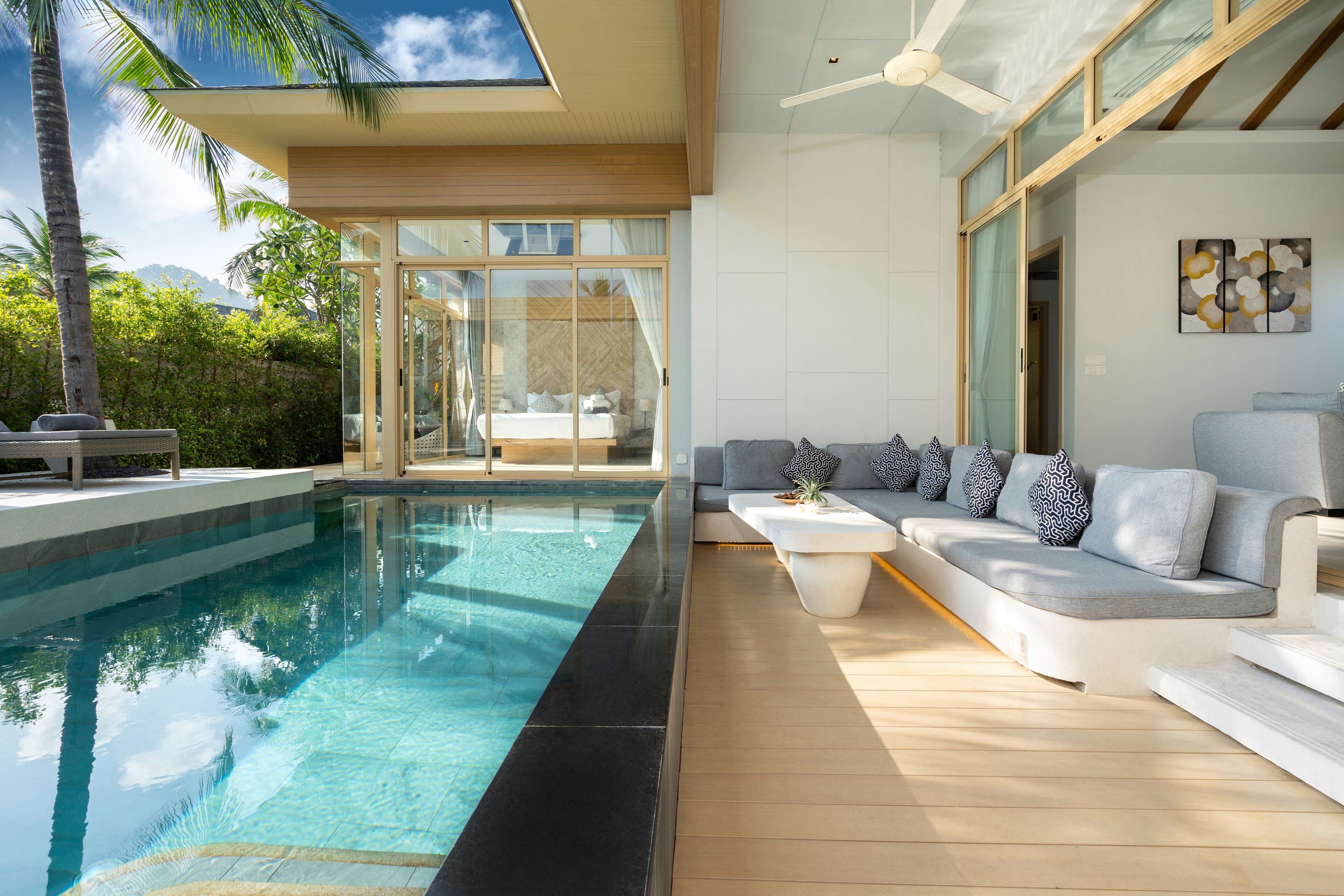 A modern indoor pool area with a glass-enclosed room, a sofa with patterned cushions, and a ceiling fan.