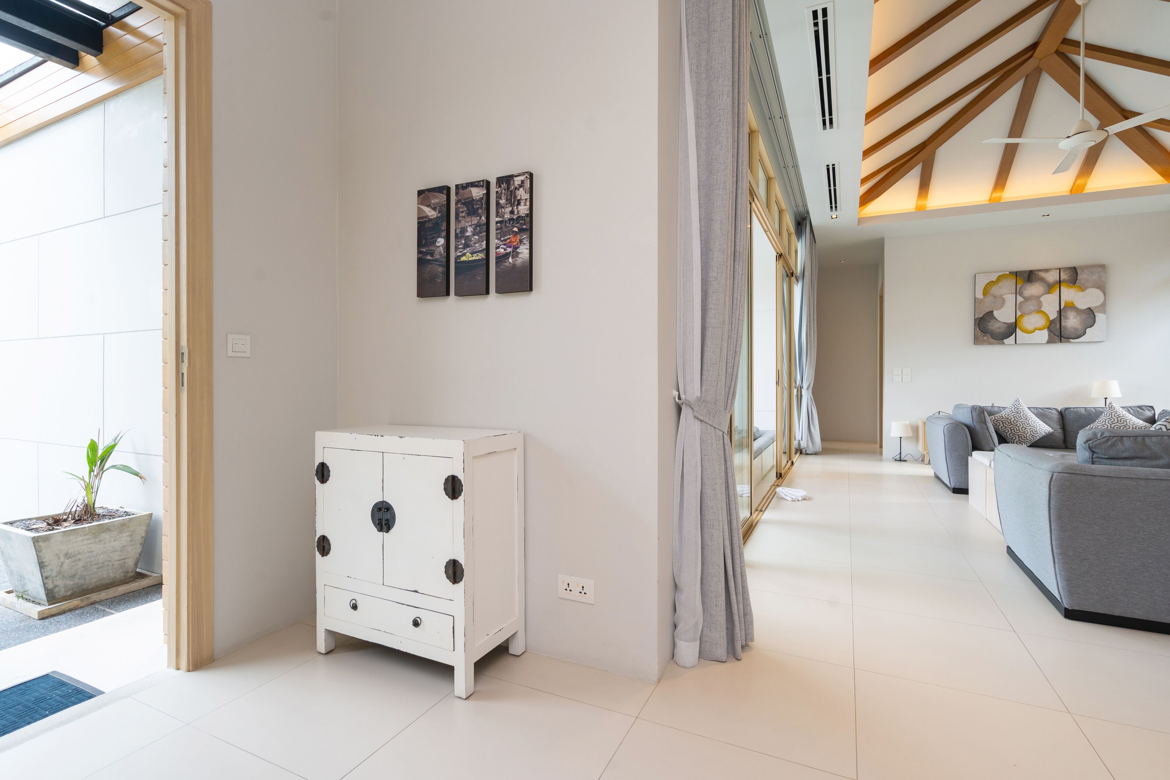 Uma sala de estar moderna com um armário branco, um sofá cinzento e uma janela grande com cortinas.