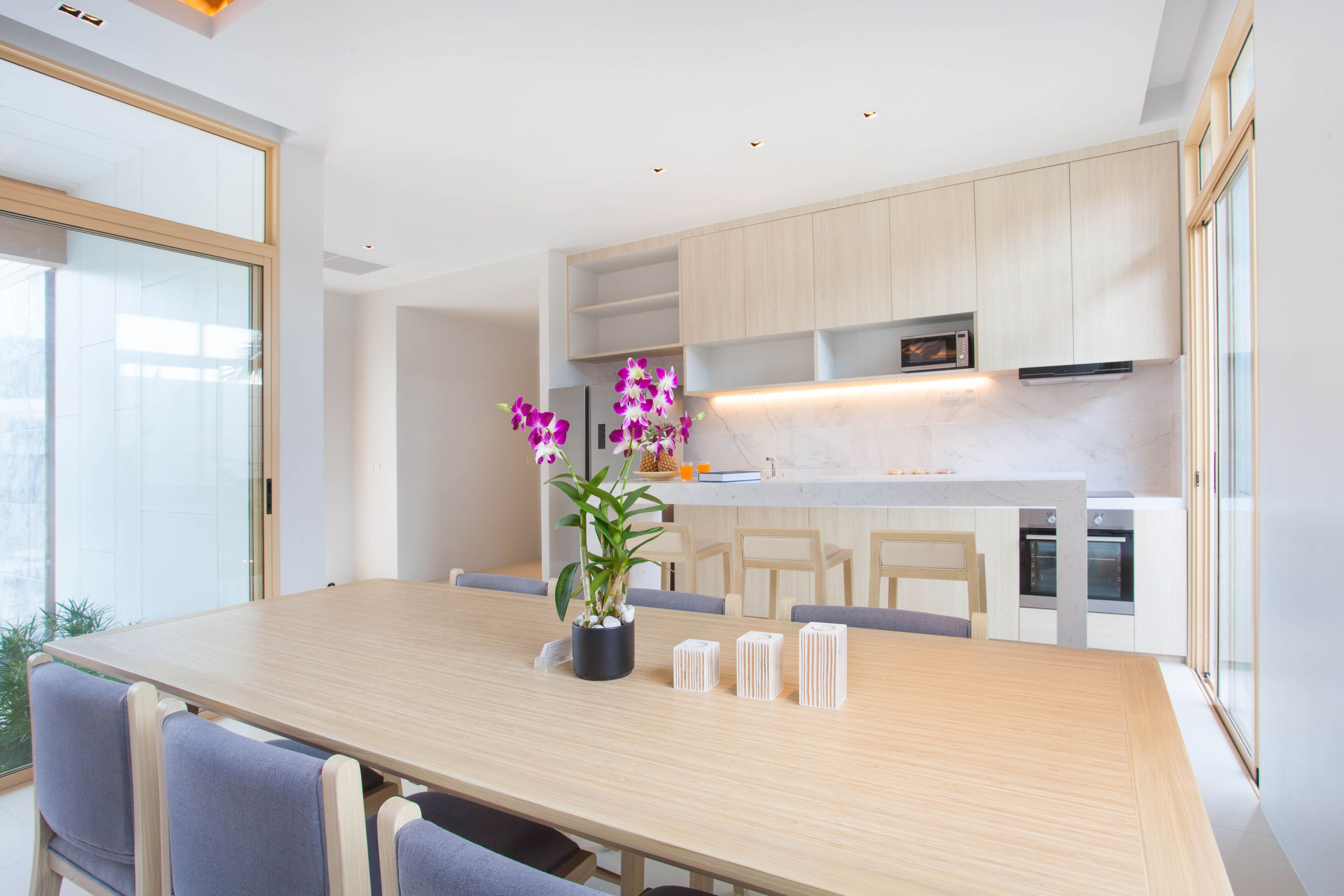 A modern kitchen with wooden cabinets, a marble countertop, and a dining area with a wooden table and chairs.