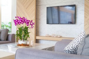 A modern living room with a flat-screen TV mounted on a marble wall, a potted orchid, and a stack of coasters on a glass table.