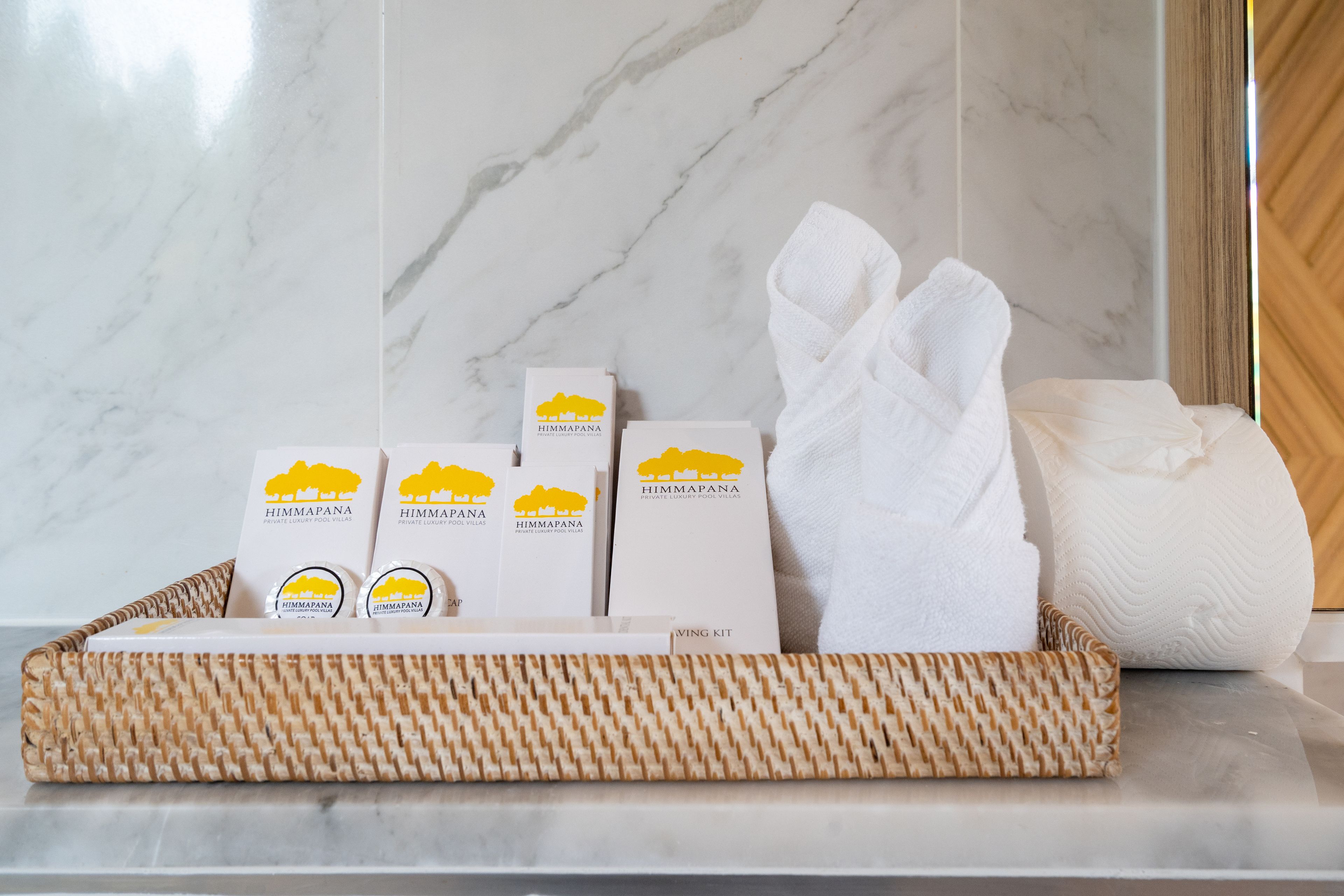 A bathroom with a marble wall, a white towel, and a wicker basket containing toiletries.