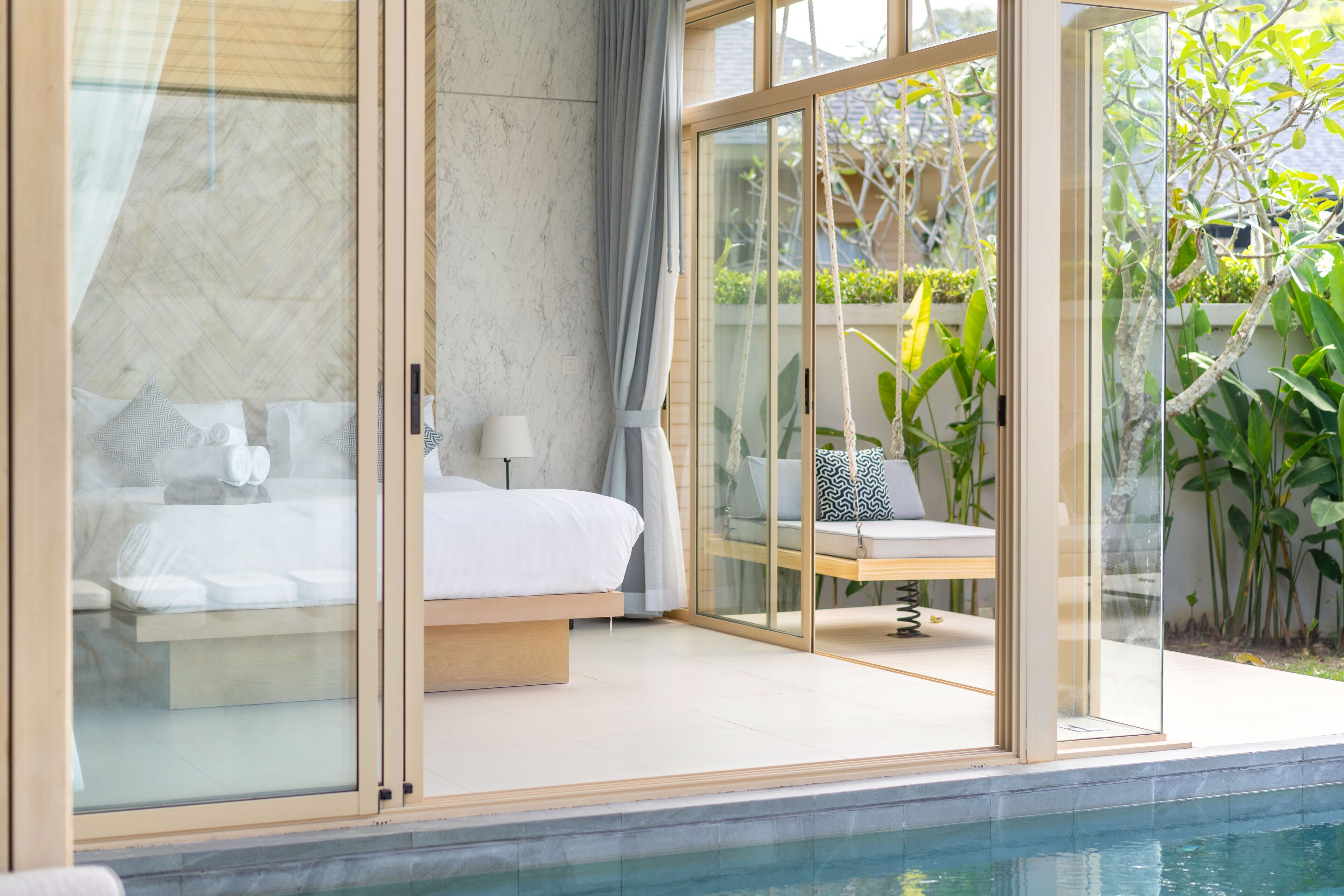 A modern bedroom with a glass door leading to a balcony, a bed, a bedside table, and a chair.