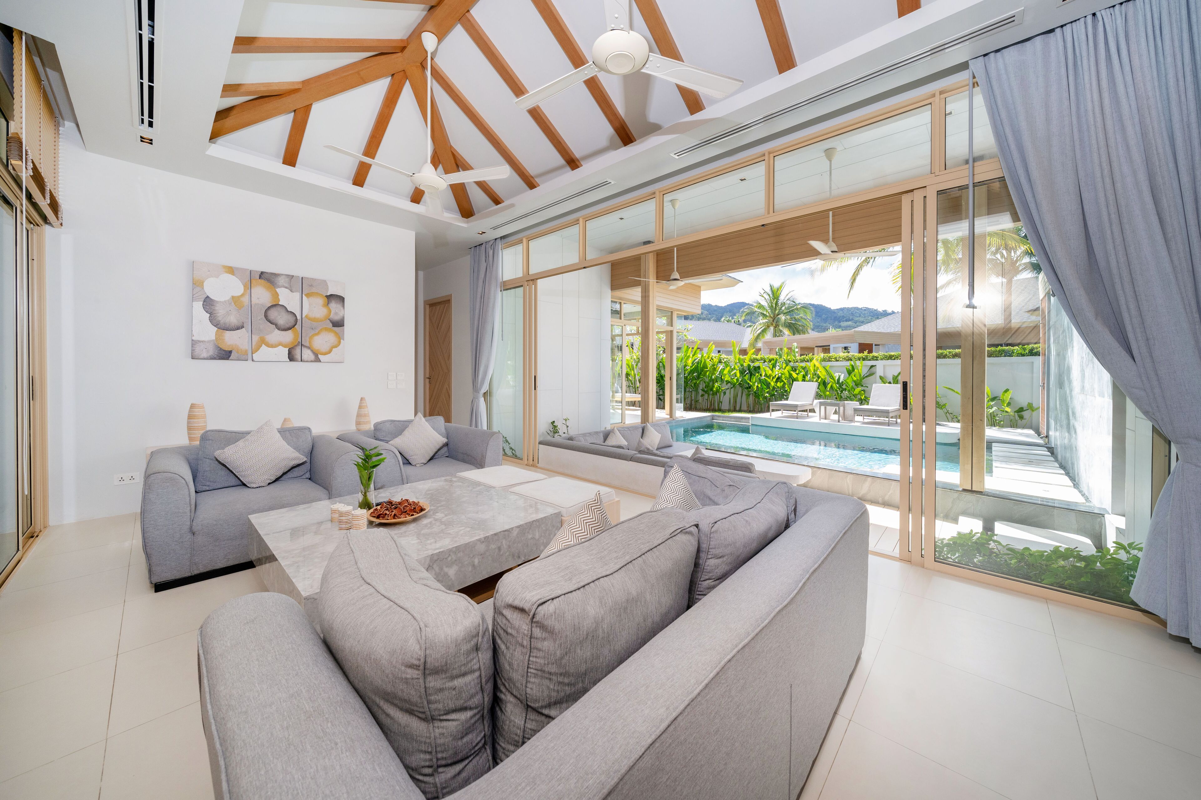 Una sala de estar moderna con un sofá gris, una mesa de centro y un gran ventanal de vidrio que da a una piscina.