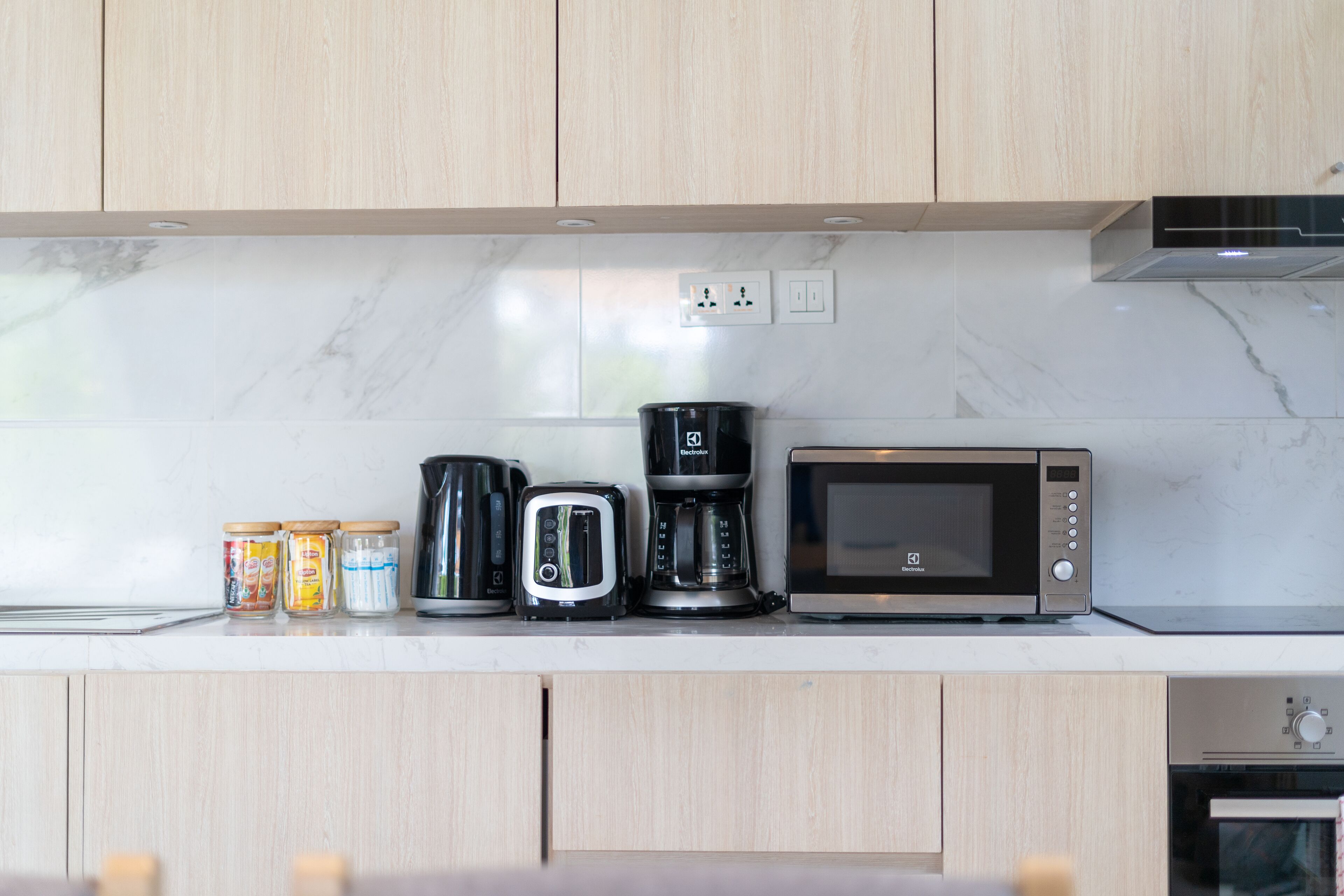 A kitchen with wooden cabinets, a marble countertop, a toaster, a coffee maker, and a microwave.
