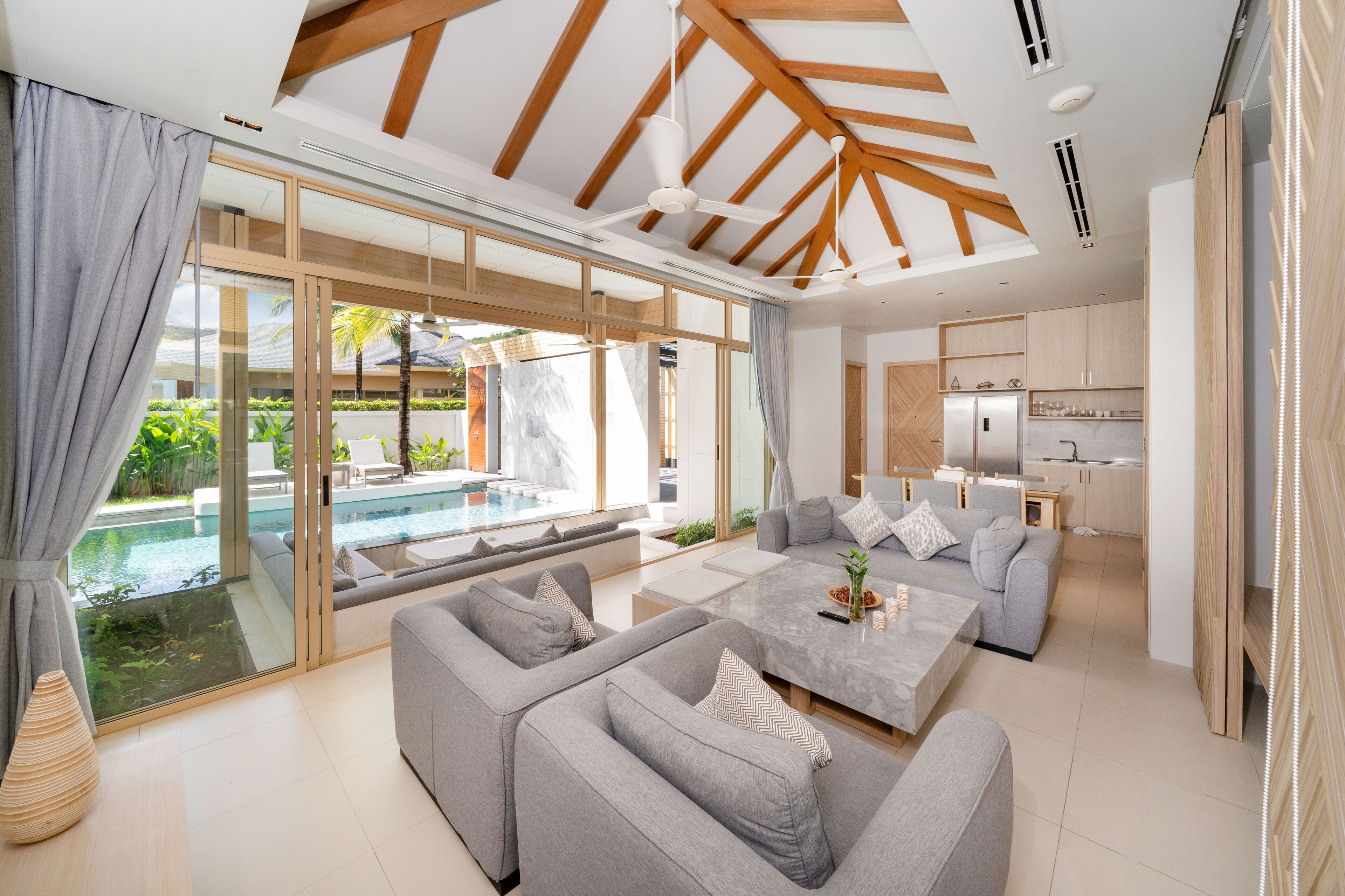 A modern living room with a large sofa, a coffee table, and a view of a swimming pool.