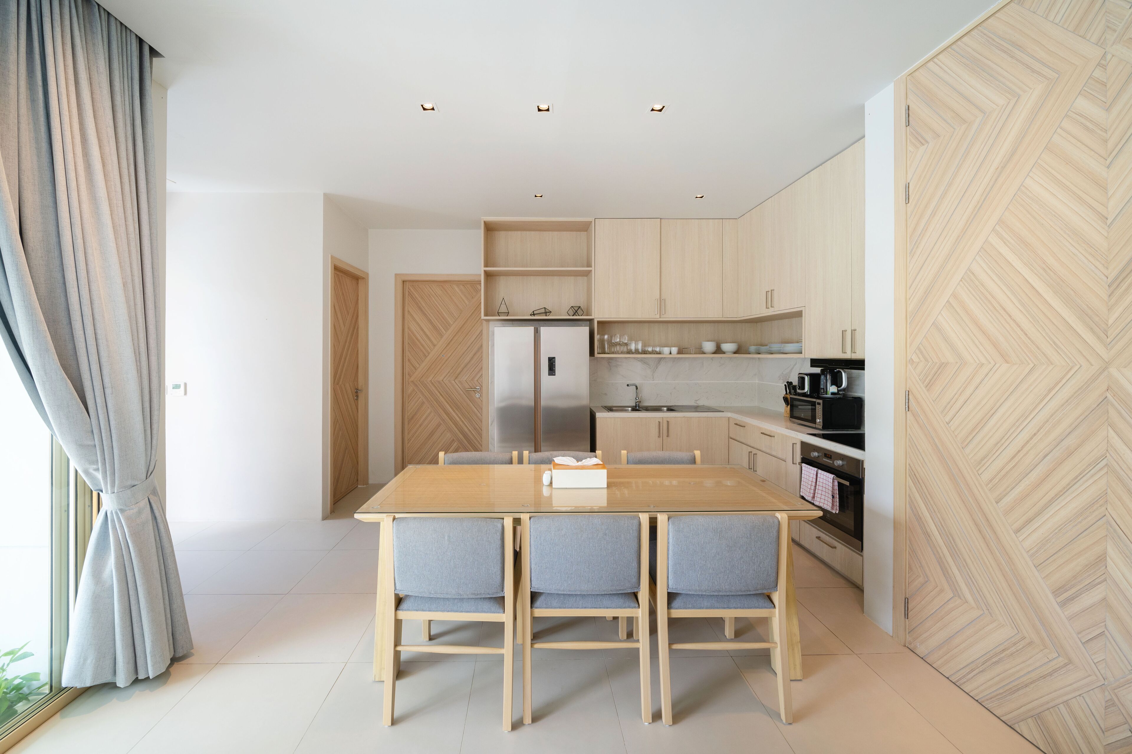 Een moderne keuken met houten kastjes, een inbouwoven en een eethoek met een houten tafel en stoelen.