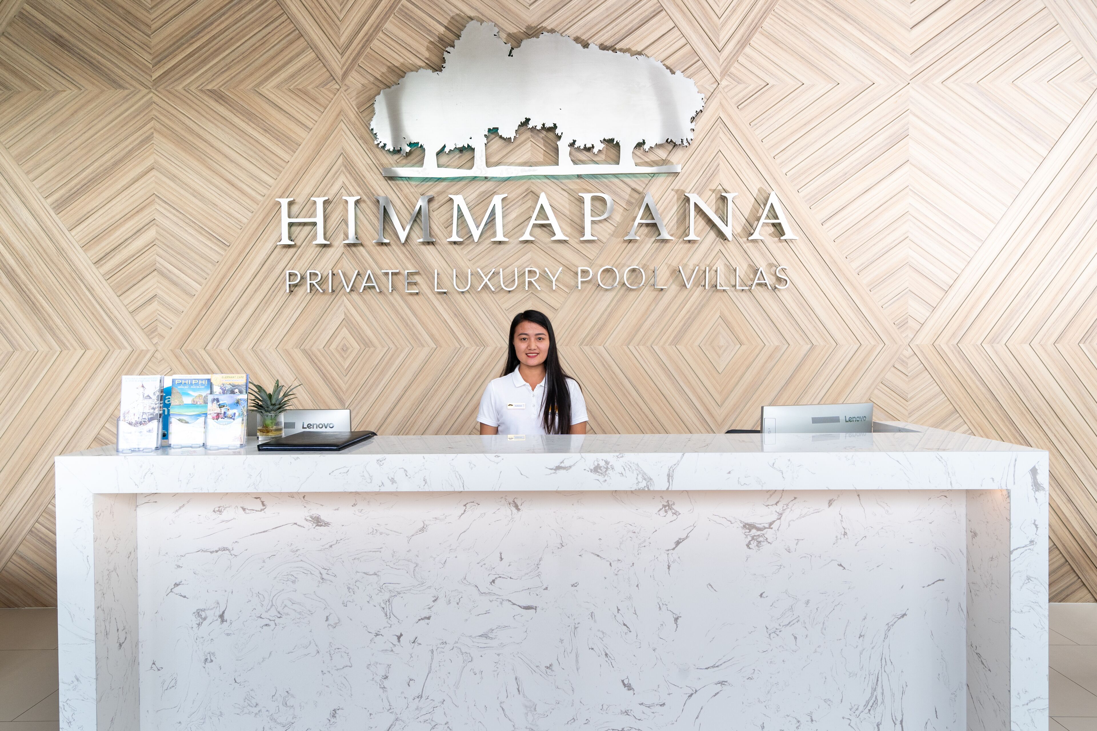 Een receptiebalie met een marmeren blad, een bord erboven met de tekst 'HIMMAPANA PRIVATE LUXURY POOL VILLAS', en een Lenovo laptop op de balie.