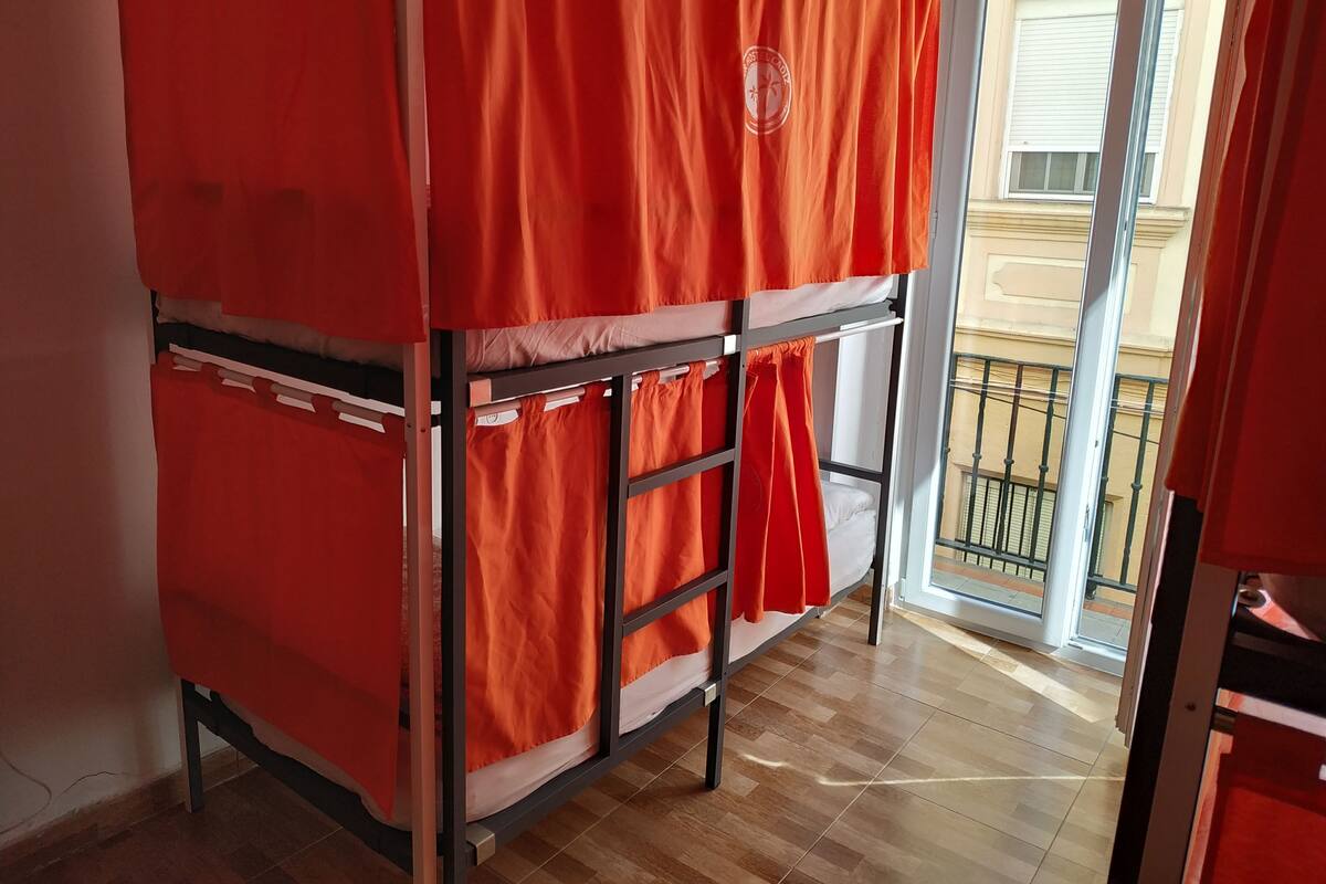 A bunk bed with orange bedding in a room with wooden flooring and a sliding glass door leading to a balcony.