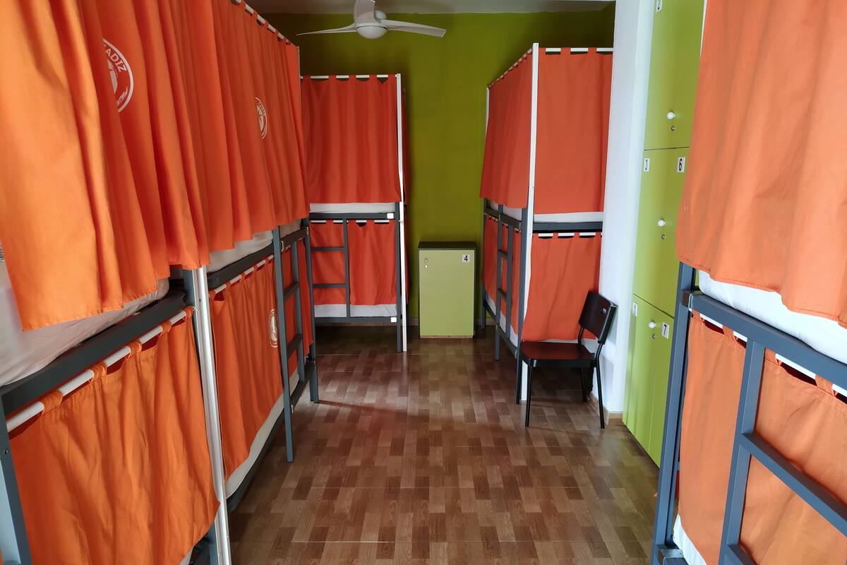 A dormitory room with bunk beds, orange curtains, a wooden floor, and lockers.