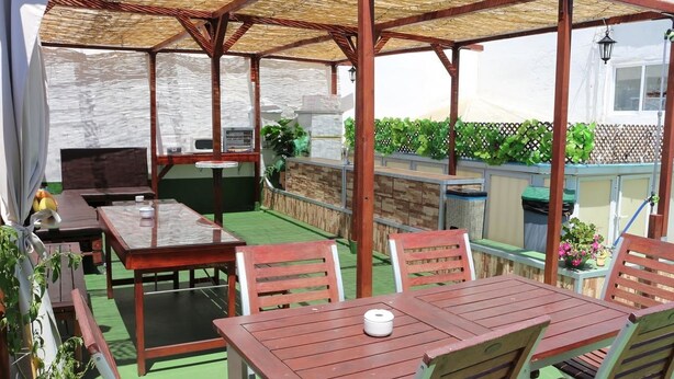 An outdoor patio with a wooden table and chairs, a grill, and potted plants. - Summer Hostel Cádiz (Cádiz)