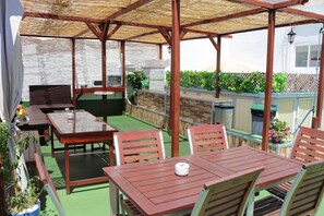 An outdoor patio with a wooden table and chairs, a grill, and potted plants. - Summer Hostel Cádiz (Cádiz)