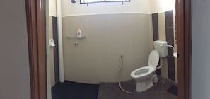 A small bathroom with a toilet, a glass shelf with a bottle, and a shower area. - Lily Homestay Kangar (Kangar)